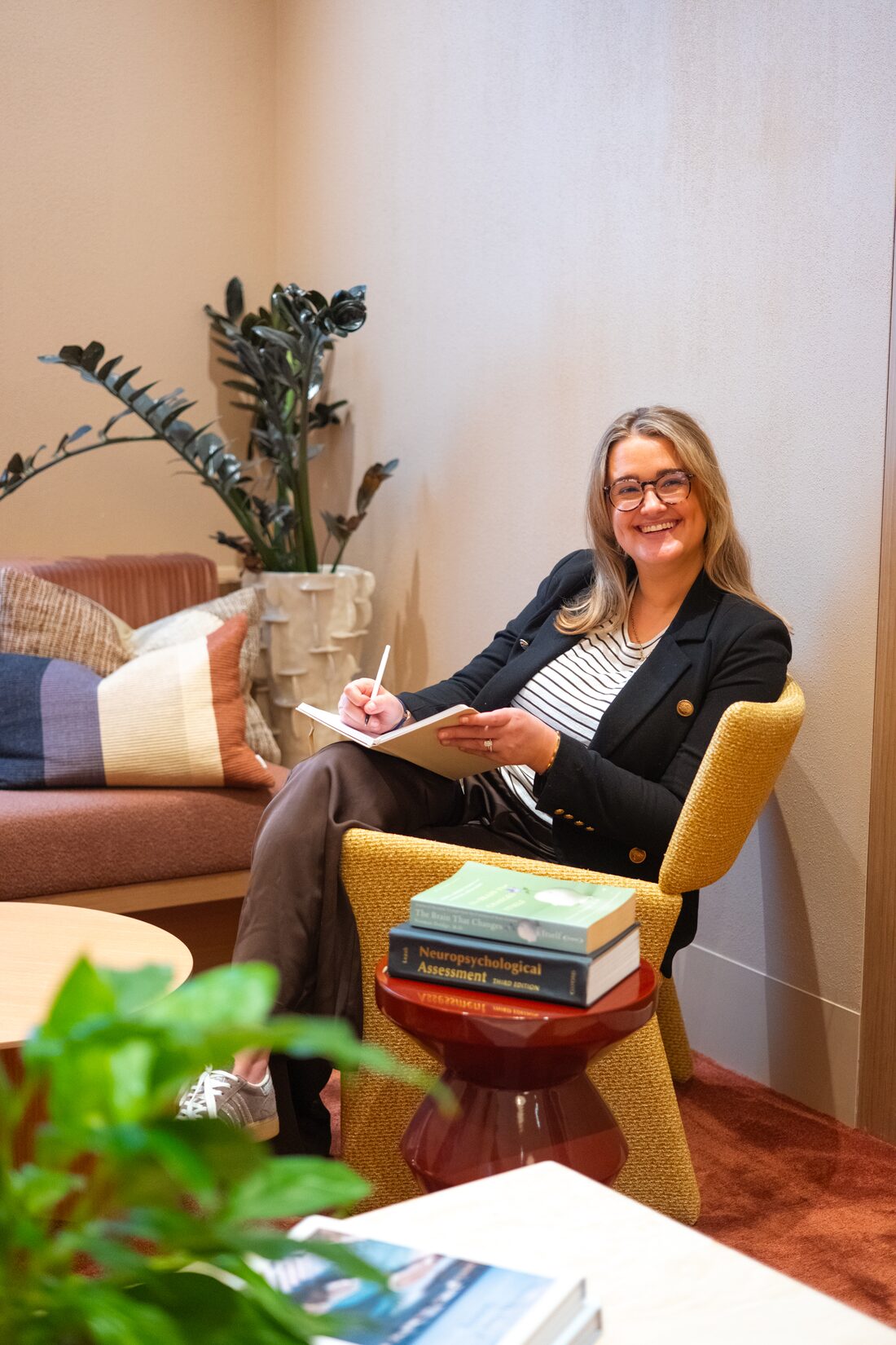 Maddy Smith smiling with a notebook, sitting in a warm lounge chair